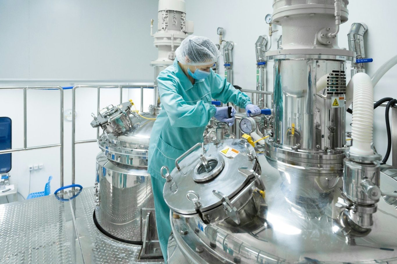 Drug Formulation A technician in protective gear works with large stainless steel equipment in a cleanroom.
