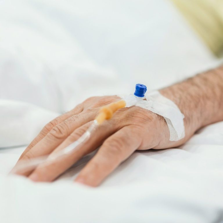 Hand with IV drip A person's hand with an intravenous line attached, resting on a hospital bed.